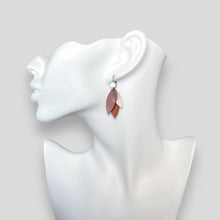 Charger l&#39;image dans la galerie, Boucles d&#39;oreilles pendantes argentées et plumes de cuir dans les tons rosés, portées à l&#39;oreille sur un buste blanc
