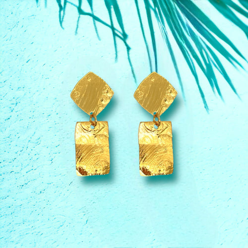 Petites puces d'oreilles losanges avec pendant rectangulaire en métal martelé doré à l'or fin, sur fond vert pastel et ombre de palmier
