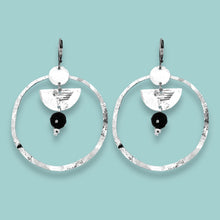 Charger l&#39;image dans la galerie, Grandes boucles d&#39;oreilles créoles en métal martelé argenté et pierres naturelles de tourmaline noire accrochée à une demi-lune, sur fond vert pastel
