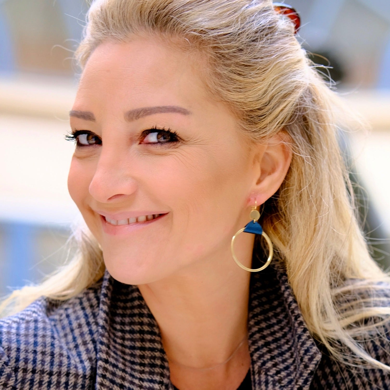 Femme blonde portant les Boucles d'oreilles dorées Cléa, grands anneaux créoles, noués par un morceau de cuir bleu nuit métallisé aux accroches dormeuses