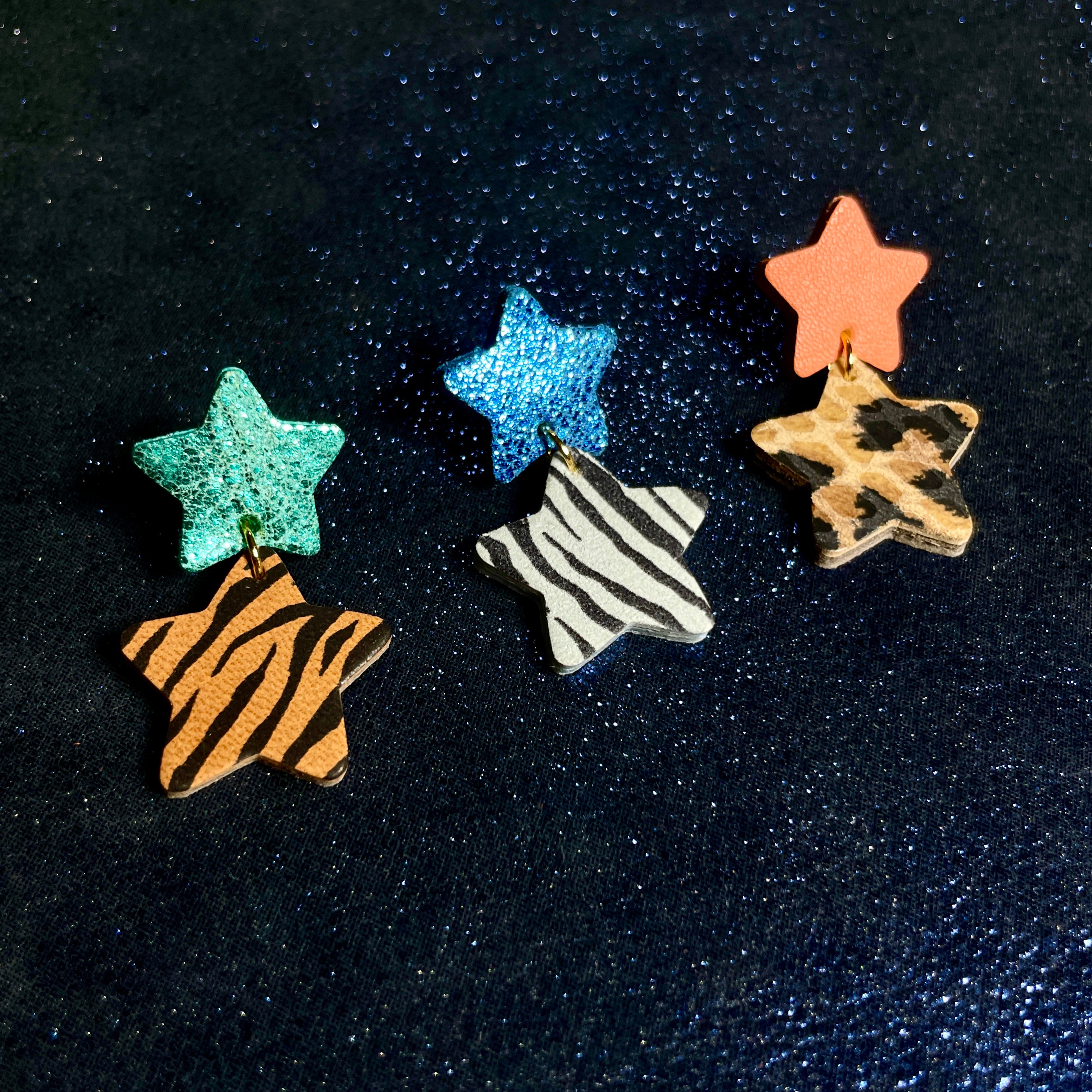 puces d'oreilles Starlettes, en forme d'étoiles tout cuir, couleurs vert émeraude brillant & zébré roux, bleu roi métallisé & zébré noir, corail rosé et léopard, sur fond noir brillant.