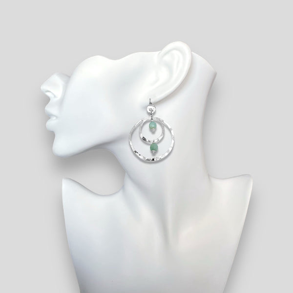 Grandes boucles d'oreilles créoles en métal martelé argenté et perles minérales naturelles d'amazonite, de forme ronde, avec doubles anneaux, portées à l'oreille sur un buste blanc