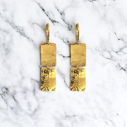 Boucles d'oreilles pendantes composées de 2 rectangles en métal martelé doré à l'or fin, sur marbre blanc