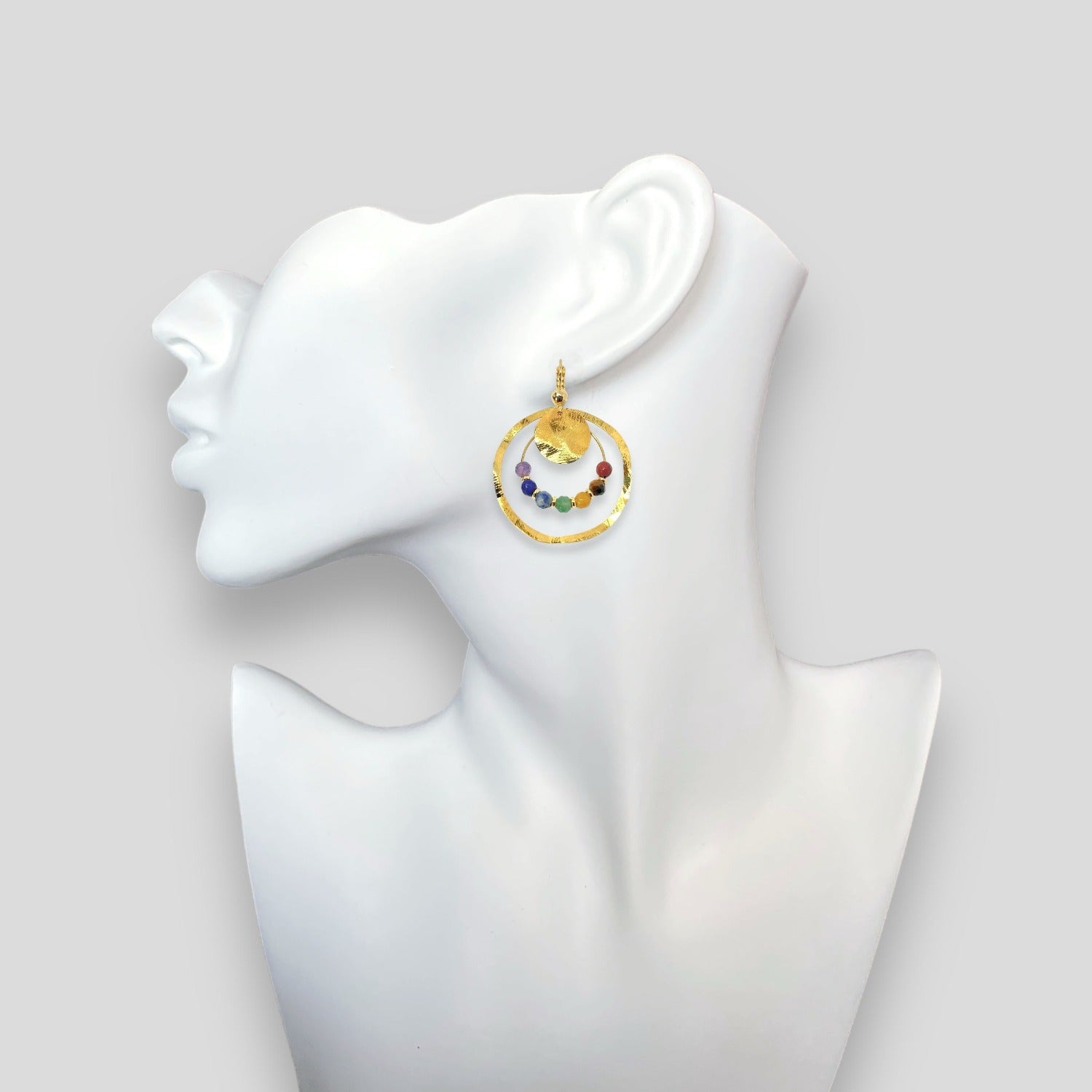Grandes boucles d'oreilles créoles dorées pendantes longues rondes avec double anneau et petites pierres naturelles multicolores des 7 Chakras, portées à l'oreille sur un buste blanc