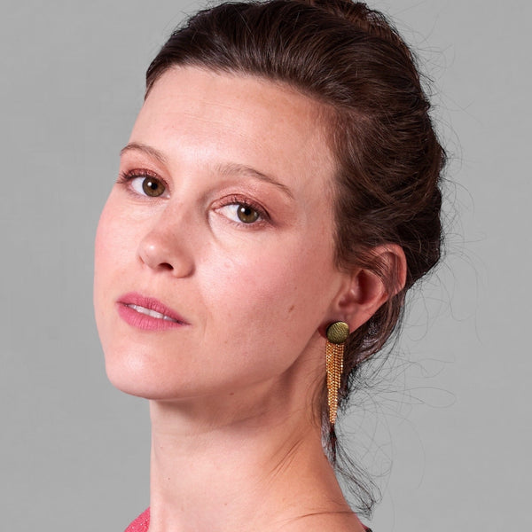 Jeune femme à chignon portant les Puces d'oreilles June, rondes et élégantes en cuir kaki métallisé avec leur cascade de fines chaînettes dorées