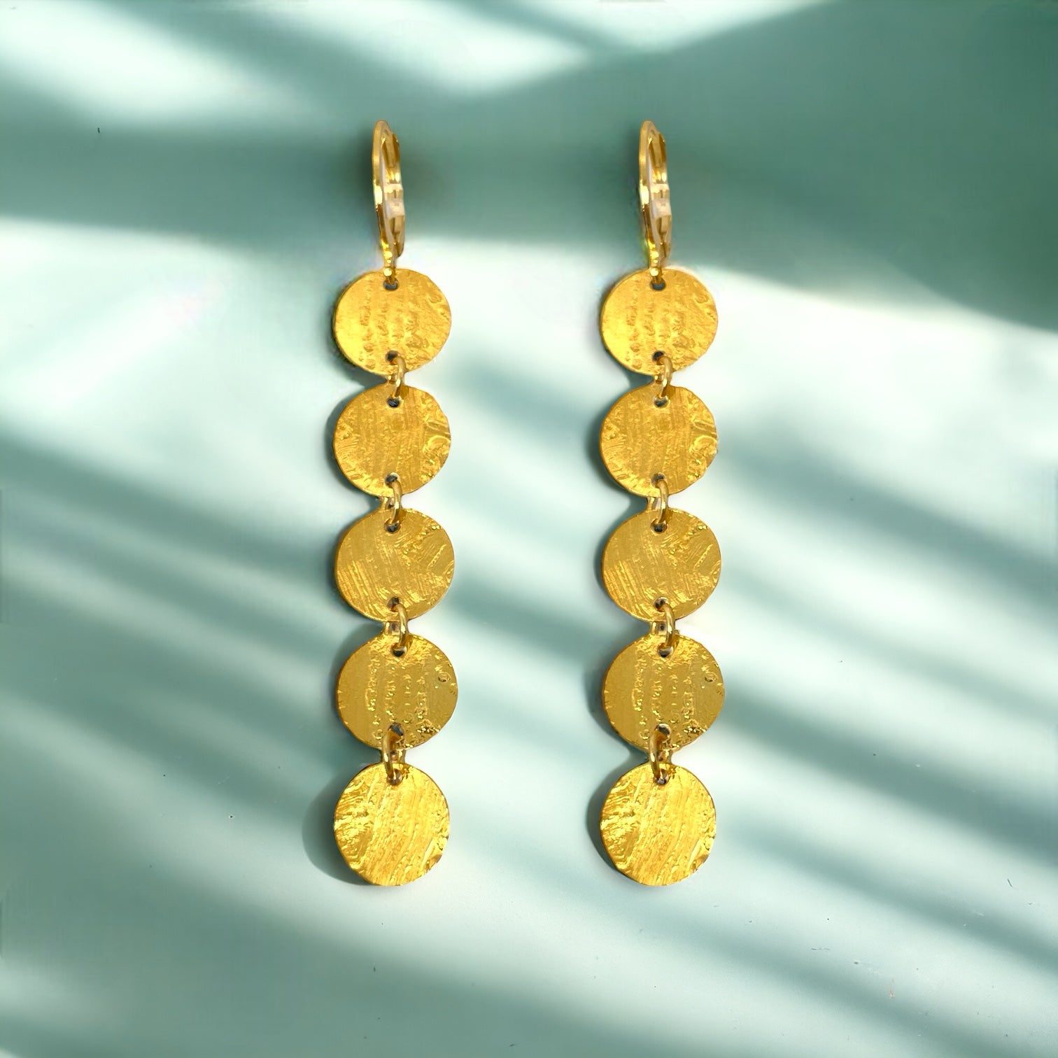 Fines longues boucles d'oreilles dorées pendantes en chapelet de 5 petits sequins ronds, sur fond vert ombragé