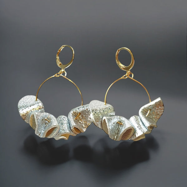 Grandes boucles d'oreilles dorées en froufrous de cuir recyclé bicolore argent brillant froissé et blanc, sur fond noir