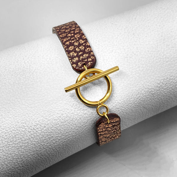 Bracelet en cuir chocolat grainé or rose vu de dessous avec fermoir en T doré, enroulé autour d'un rouleau de cuir blanc