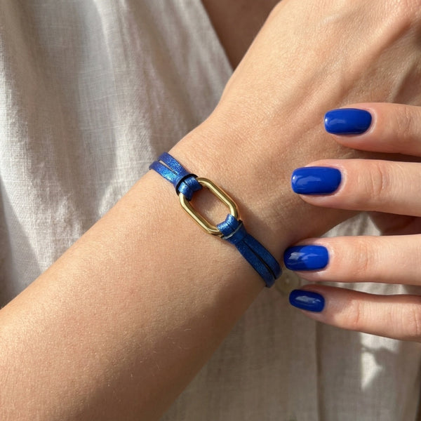 Bracelet à boucle dorée en fins liens de cuir bleu cobalt métallisé, porté au pognet