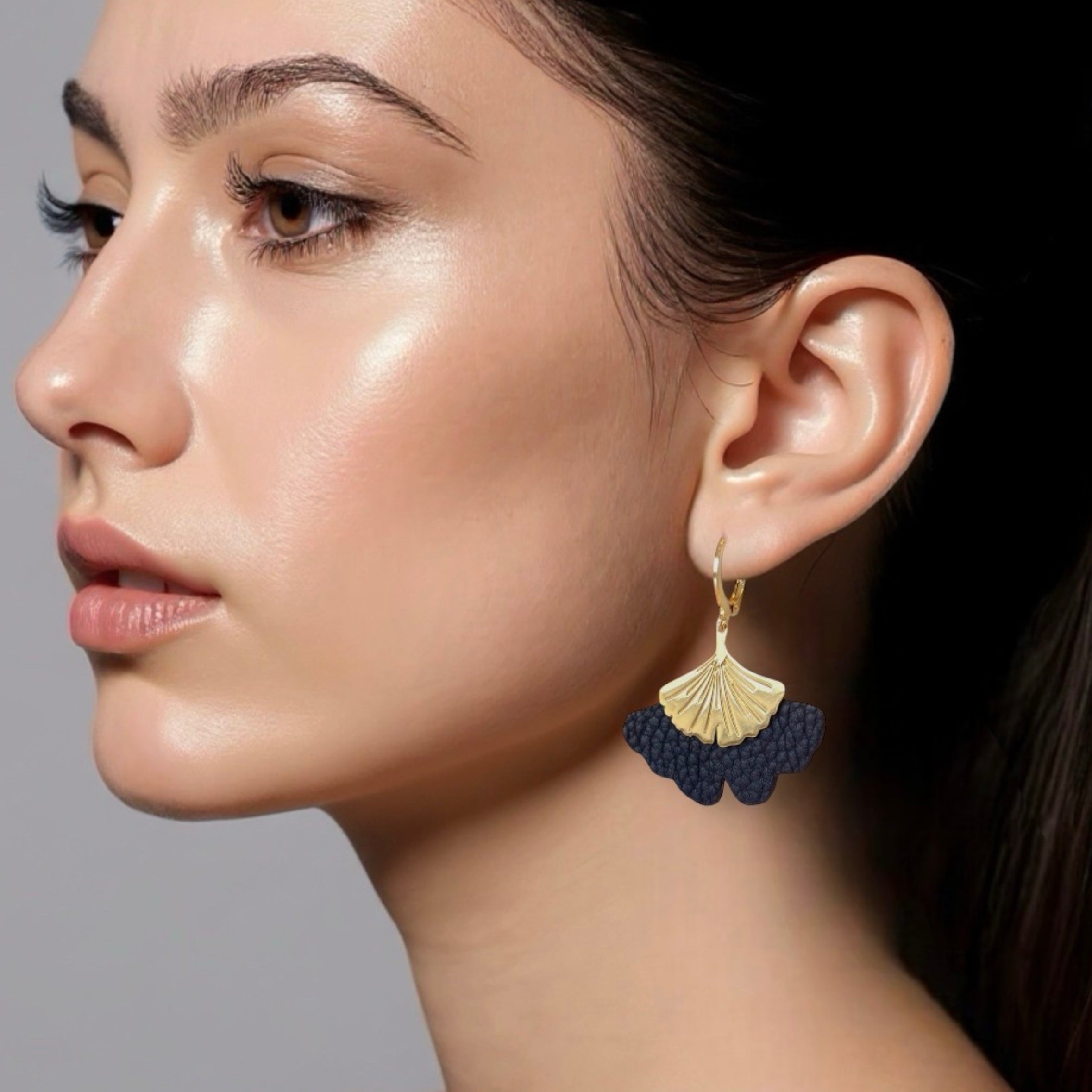 Boucles d'oreilles dorées pendantes en cuir bleu nuit grainé en forme de gingko, portées aux oreilles