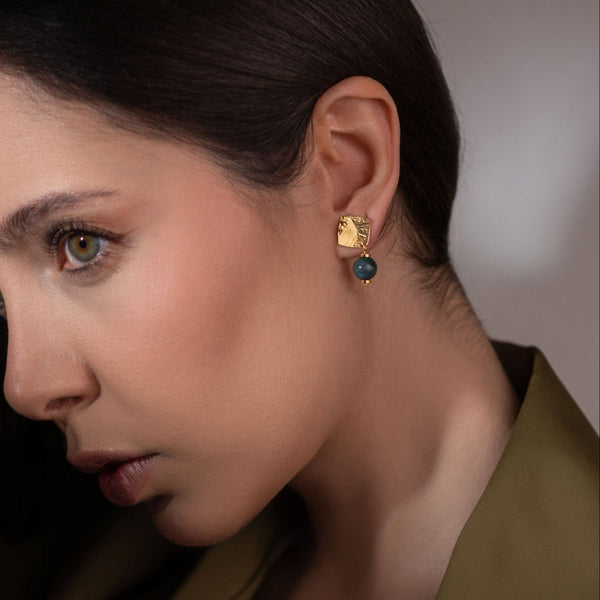Petites boucles d'oreilles puces losanges en métal martelé doré à l'or fin et perles de jaspe océan vert foncé, portées à l'oreille  par une femme brune