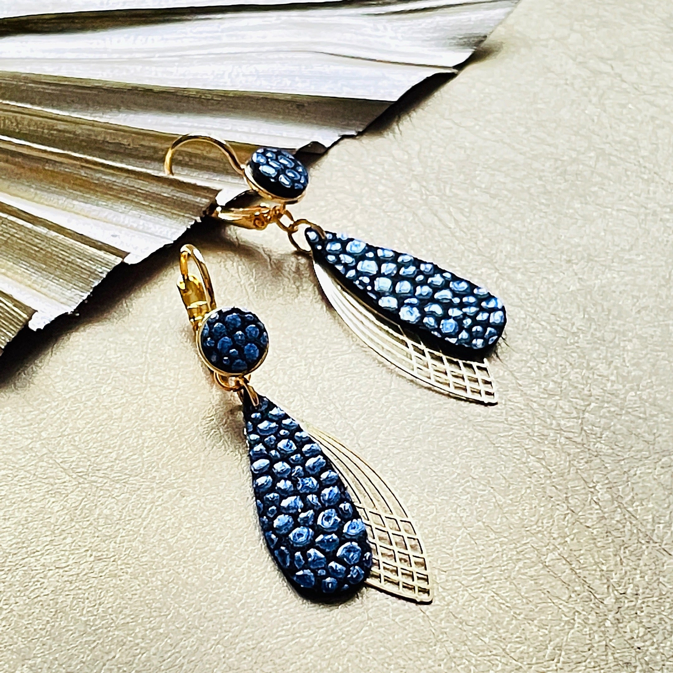 Boucles d'oreilles dorées Nune modèle Pétales en cuir bleu nuit grainé irisé sur fond cuir mordoré