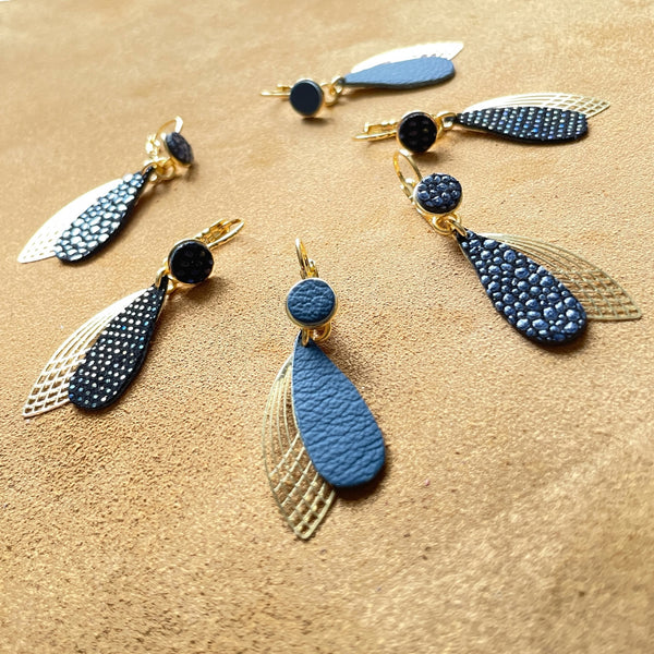 boucles d'oreilles dorées Nune modèle Pétales en cuirs bleu nuit mat, bleu nuit grainé irisé, et noir grainé irisé sur fond daim velours