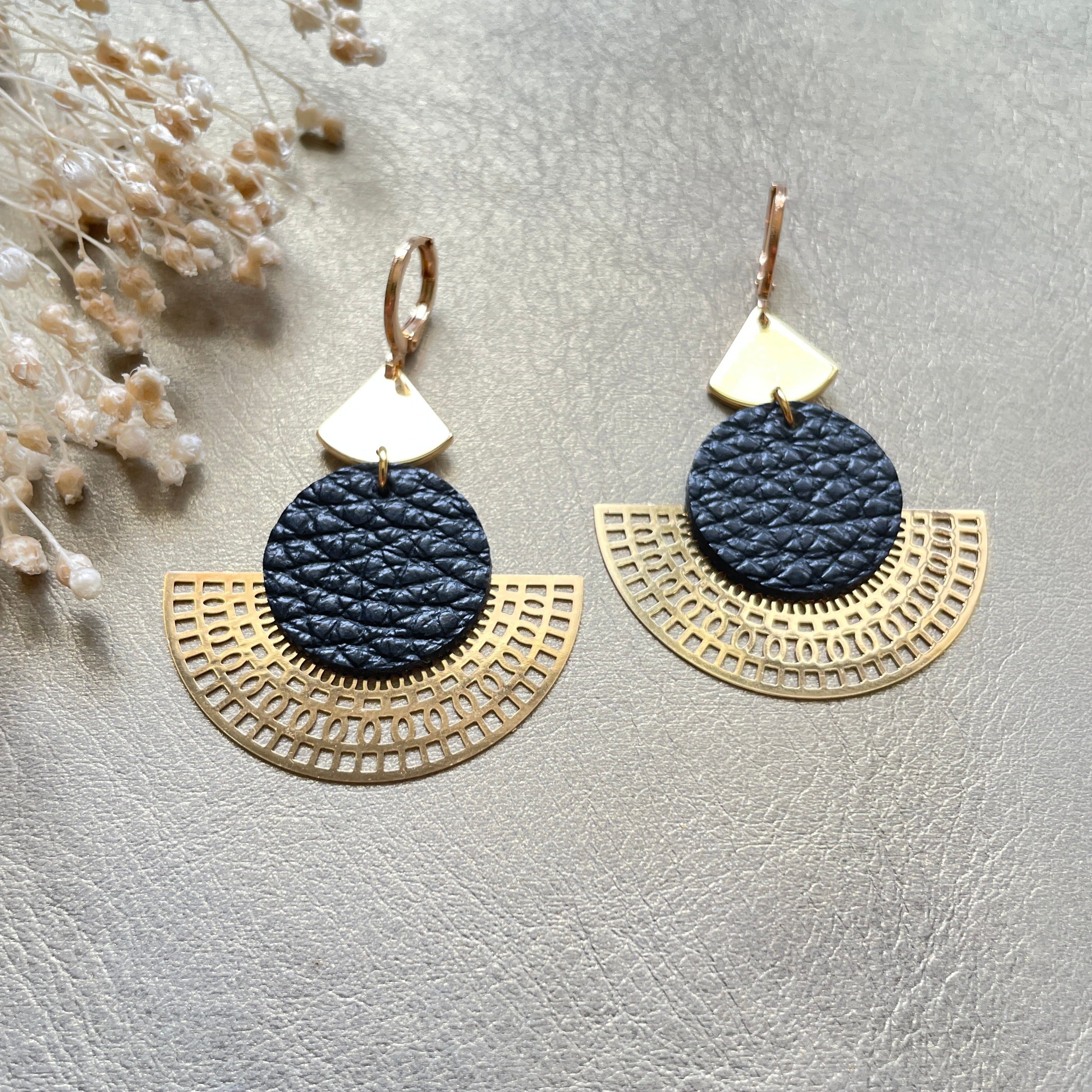 Boucles d'oreilles dorées Nune modèle Ephésia en cuir noir grainé sur fond gris doré