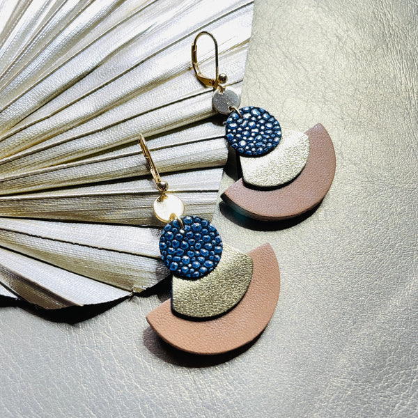 boucles d'oreilles dorées Nune modèle Hestia en cuirs beige amande, bleu nuit grainé irisé et doré satiné sur fond gris doré