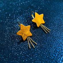 Charger l&#39;image dans la galerie, boucles d&#39;oreilles dorées Nune modèle Stella en forme d&#39;étoiles, en cuir orange métallisé, sur fond noir paillettes
