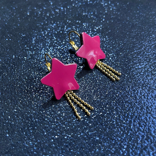 boucles d'oreilles dorées Nune modèle Stella en forme d'étoiles, en cuir rose fushia vernis, sur fond noir paillettes