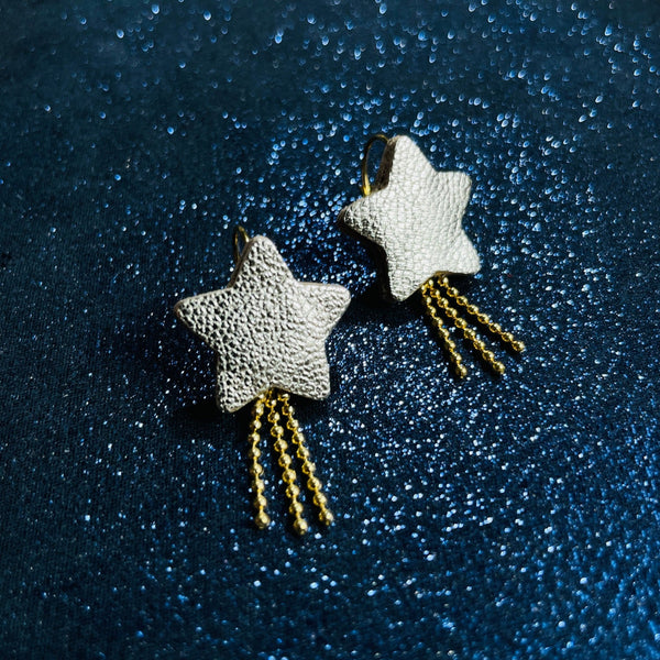 boucles d'oreilles dorées Nune modèle Stella en forme d'étoiles, en cuir argent, sur fond noir paillettes