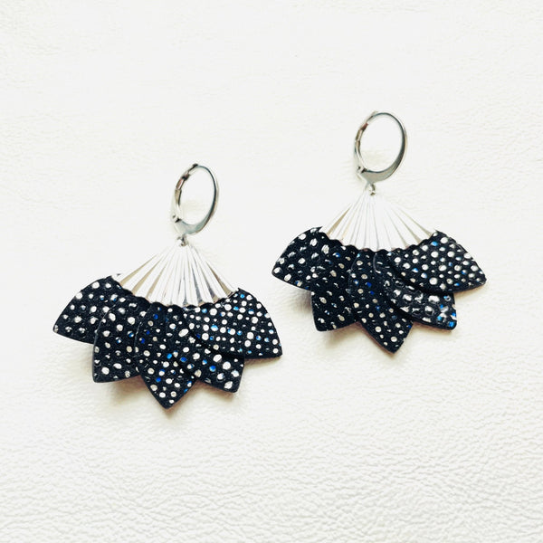 Boucles d'oreilles argentées Nune modèle Sakura en pétales de cuir noir à pois argent, sur fond cuir blanc
