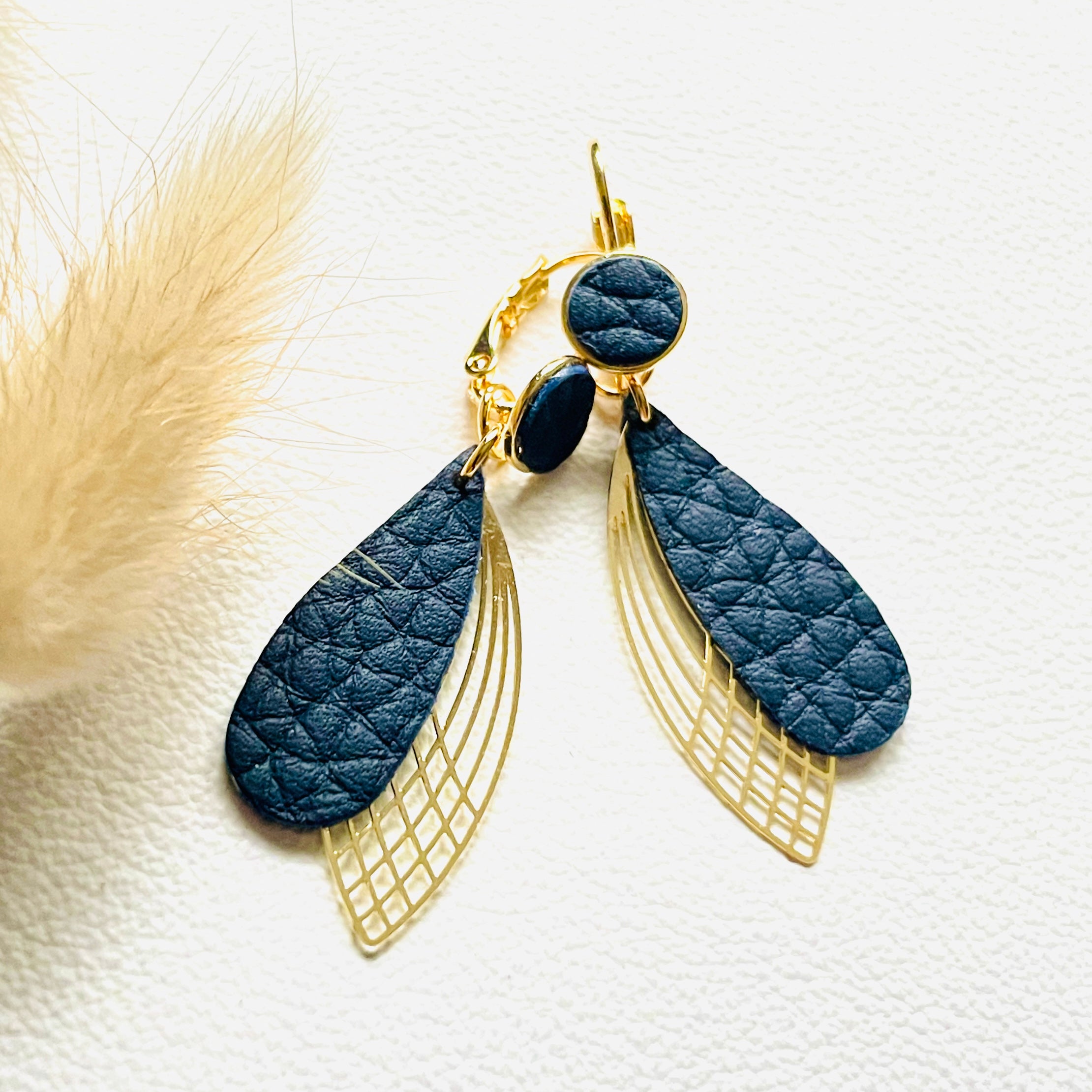 Boucles d'oreilles dorées Nune modèle Pétales en cuir noir grainé sur fond blanc