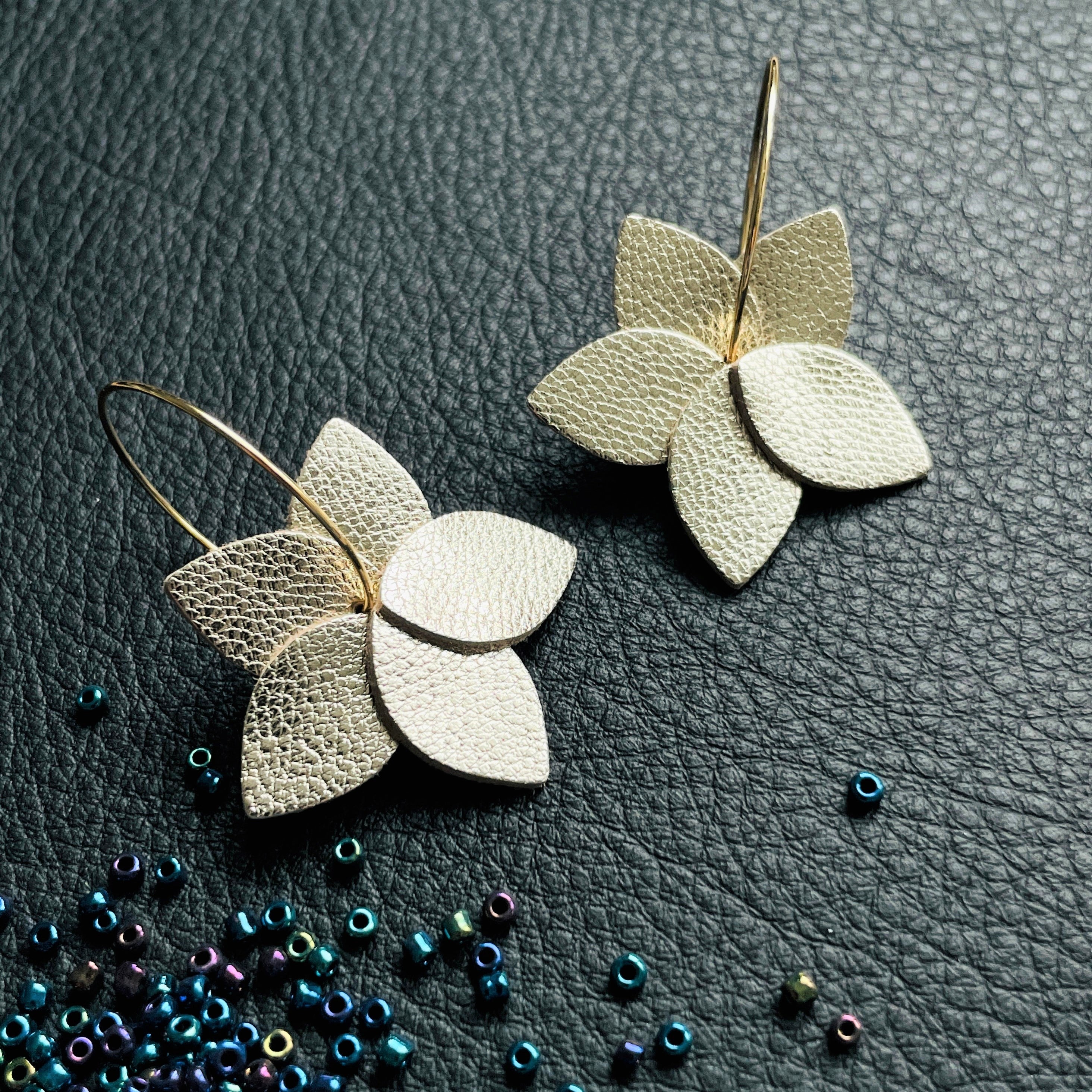 Nune petites boucles d'oreilles créoles Jasmin en cuir argent recyclé et anneaux dorés, vues de dessus, sur fond de cuir noir grainé