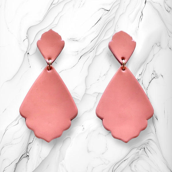 paire de boucles d'oreilles vieux rose vernis de style rétro baroque, sur fond marbre blanc