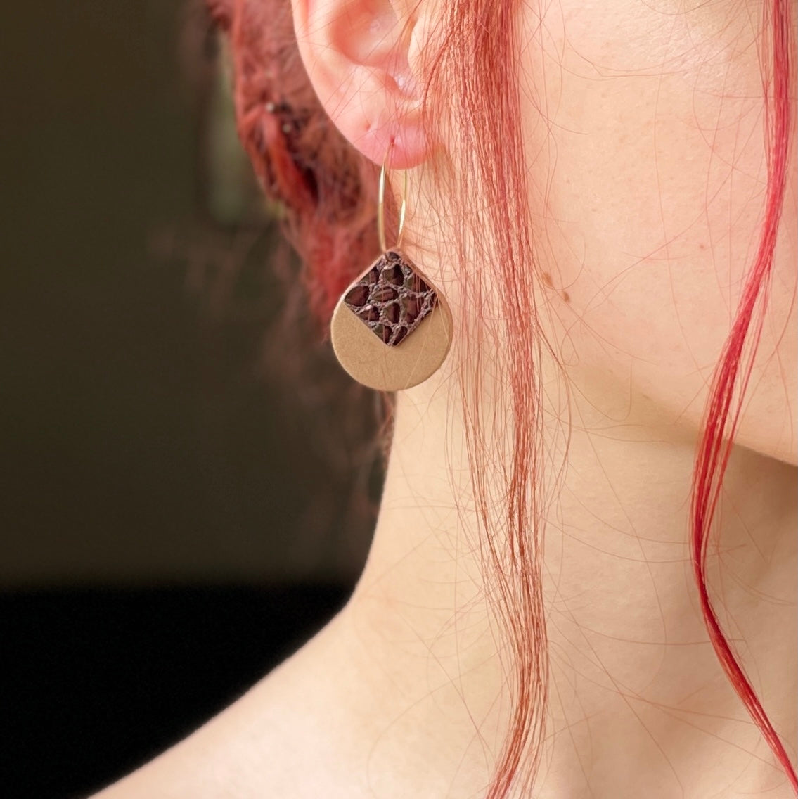 boucle d'oreille dorée Nune modèle Héra en cuirs beige amande et chocolat brillant façon croco portée par un modèle aux cheveux rouges et au teint pâle