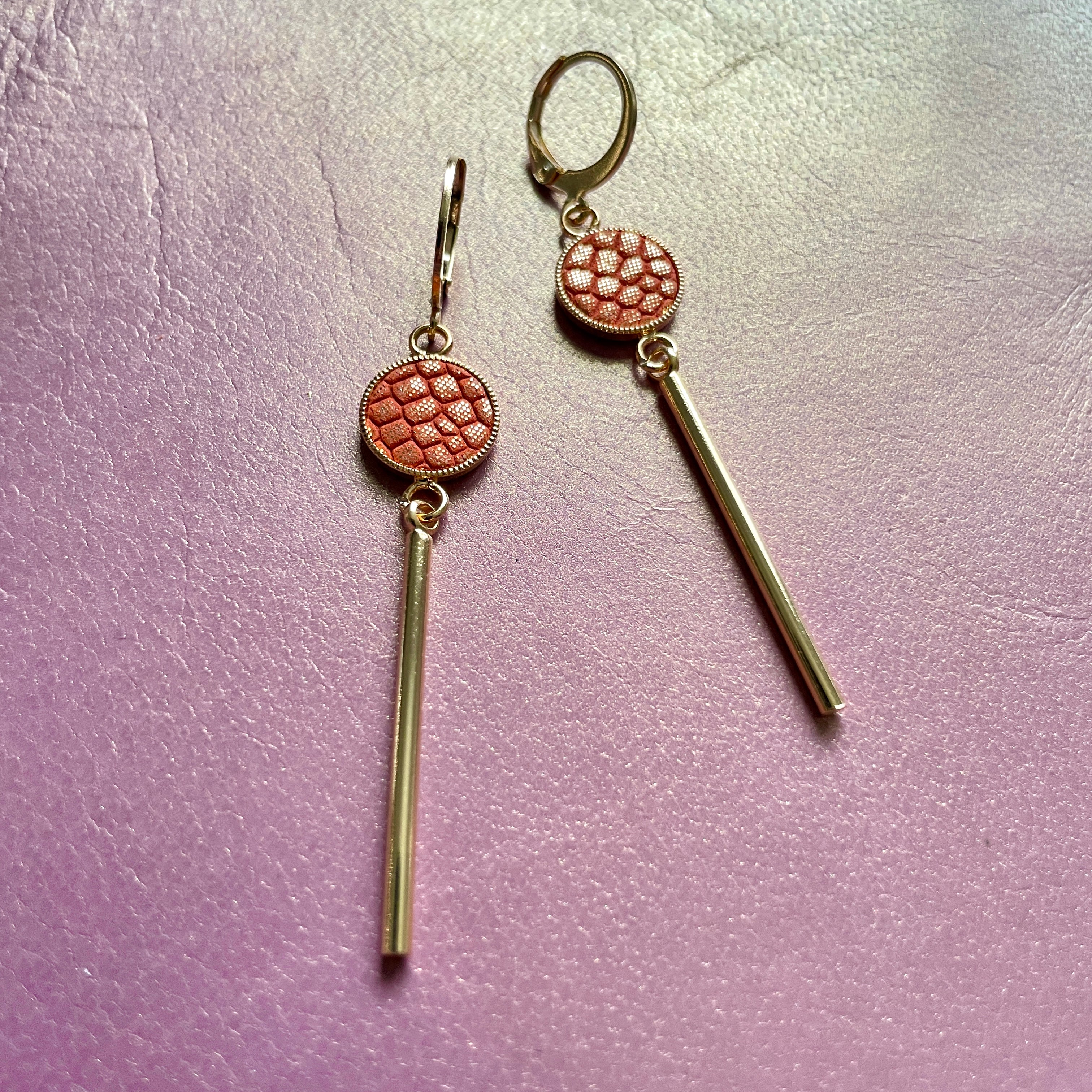 Nune longues et fines boucles d'oreilles dorées Nida avec serti en cuir orangé or façon serpent, sur fond cuir mauve irisé