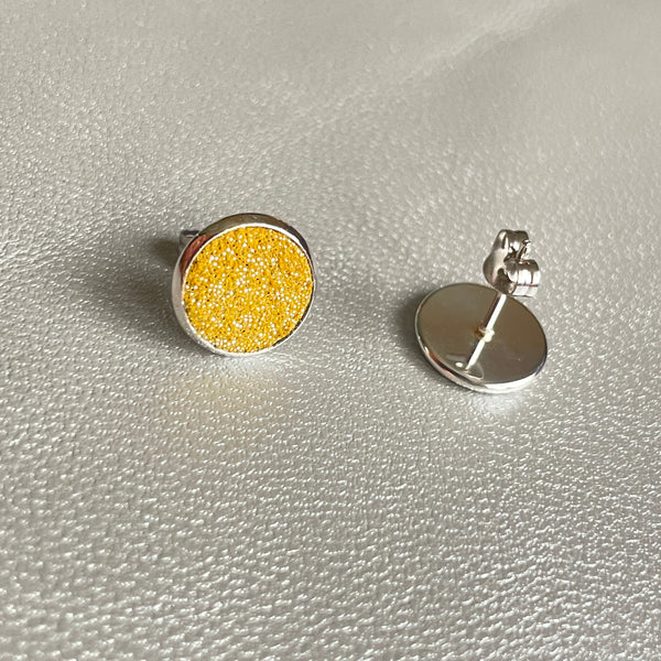 Puces d'oreilles argentées rondes Nune modèle Ilis argenté pailleté avec pastilles de cuir safran pailleté argent, sur fond de cuir gris métallisé