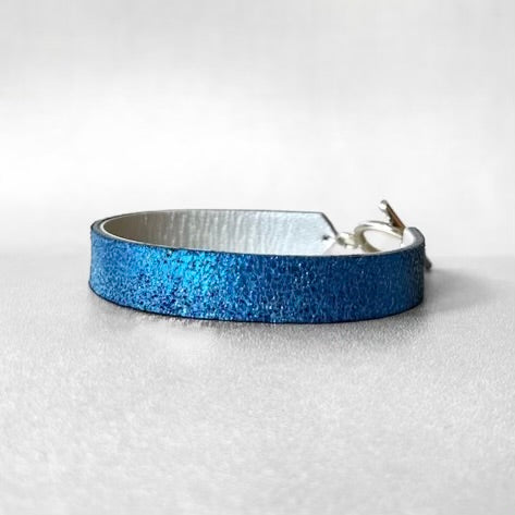 Bracelet en cuir double face bicolore, avec cuir bleu roi métallisé au recto et gris métallisé au verso avec fermoir boucle argentée en T, sur fond gris