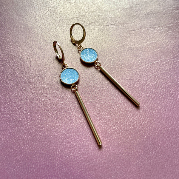 Nune longues et fines boucles d'oreilles dorées Nida avec serti en cuir topaze pailleté, sur fond cuir mauve irisé