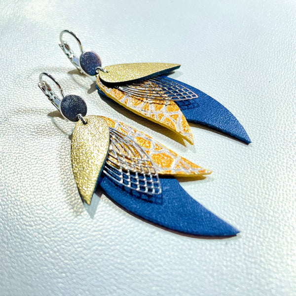 Boucles d'oreilles argentées Nune en forme de plumes, modèle Ara en cuirs doré satiné, doré patiné façon croco et bleu marine satiné sur fond blanc