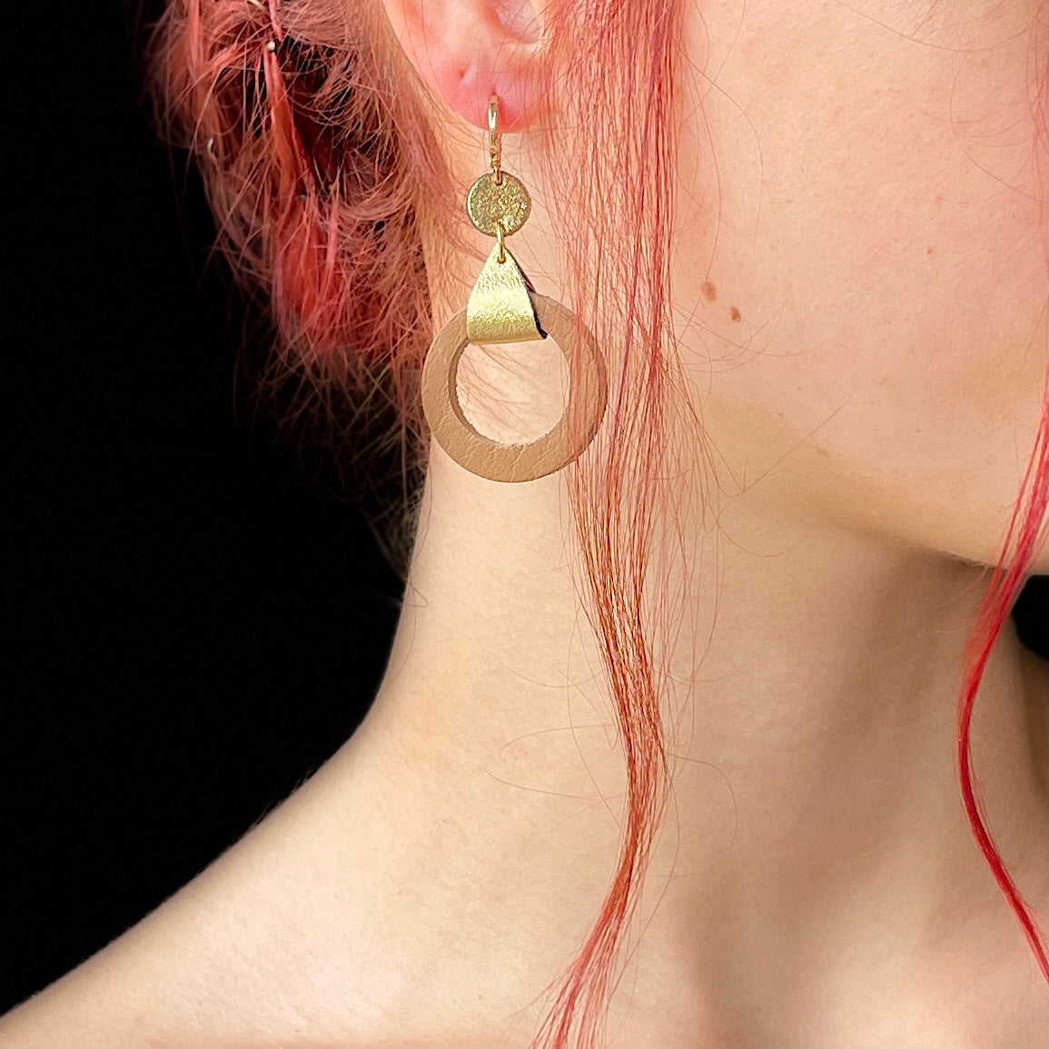 boucle d'oreille dorée Nune modèle Cyllène en cuirs beige amande et doré satiné portée par un modèle aux cheveux rouges et au teint pâle