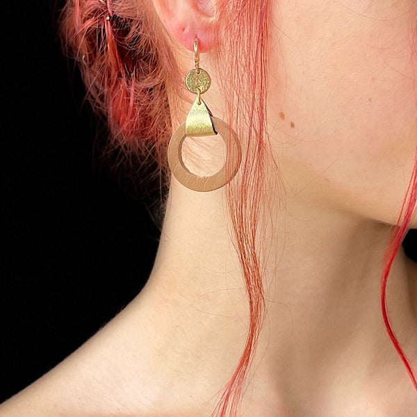 boucle d'oreille dorée Nune modèle Cyllène en cuirs beige amande et doré satiné portée par un modèle aux cheveux rouges et au teint pâle