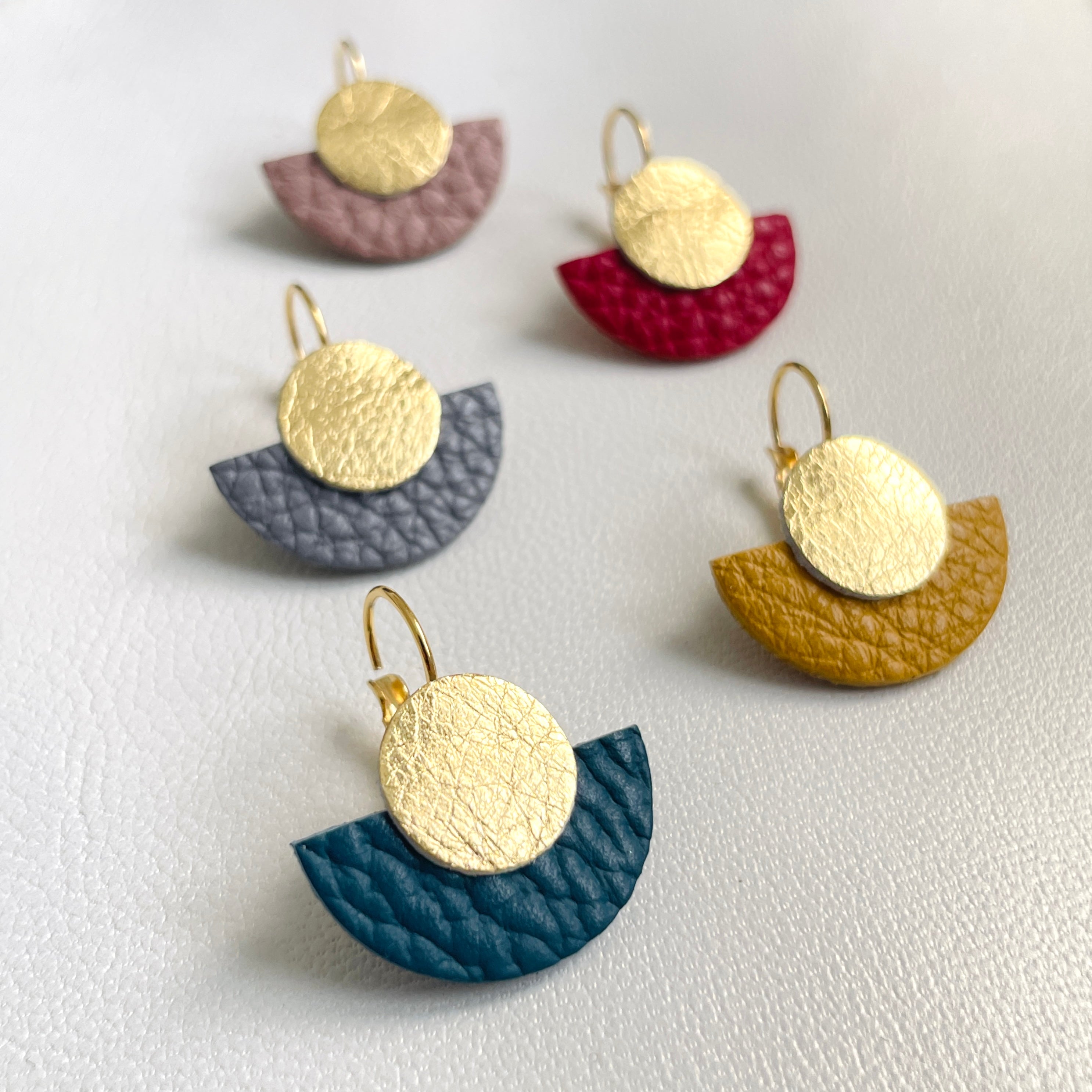 6 boucles d'oreilles dorées en forme de demi-lune déclinées en 6 couleurs de cuirs recyclés, sur fond gris