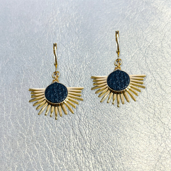 Petites boucles d'oreilles dorées Nune modèle Miria en acier inoxydable et laiton doré à l'or fin avec serti en cuir noir grainé, posées sur du cuir beige doré