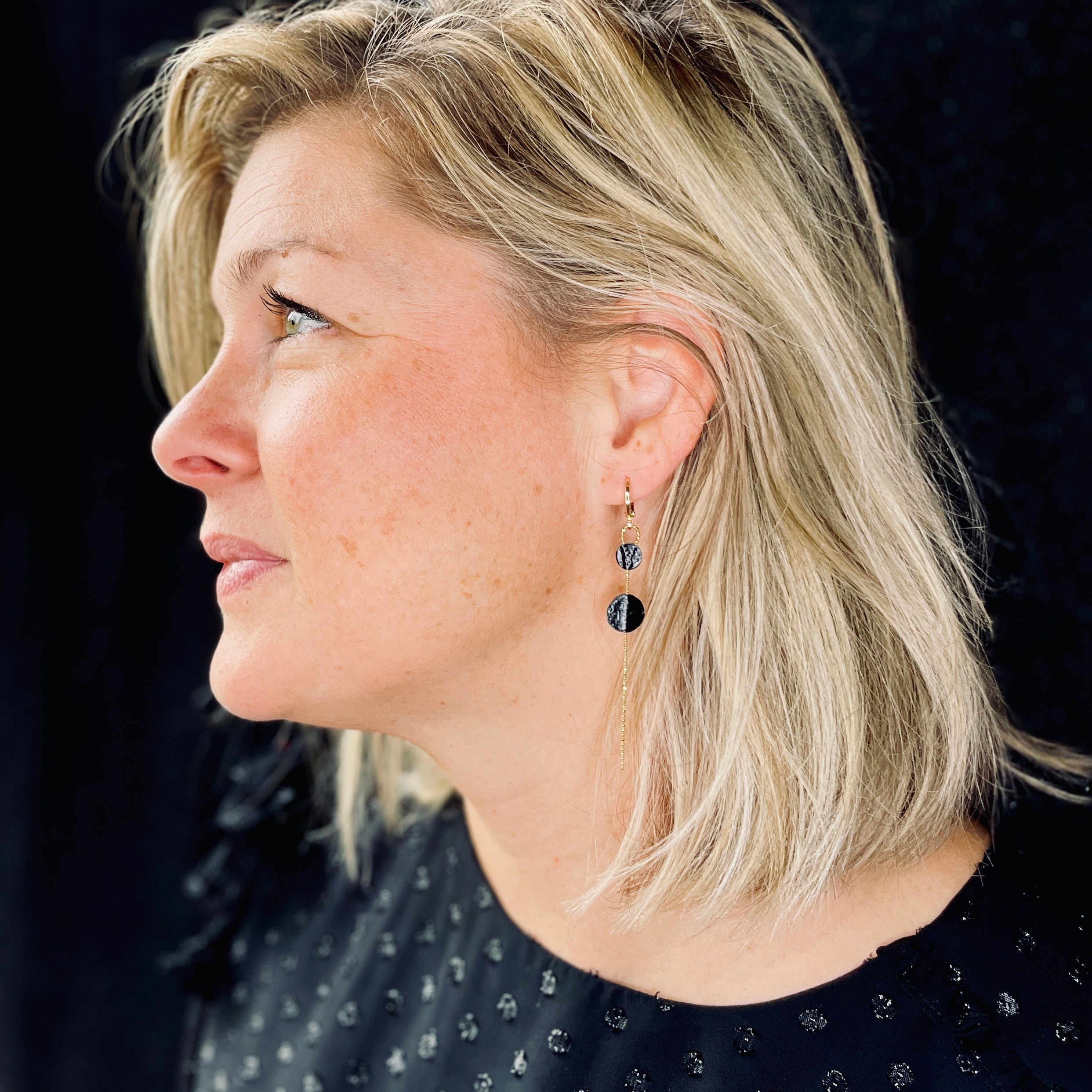 Fine boucle d'oreille Lyre de Nune, dorée à l'or fin avec petites pastilles de cuir marin, cuir de poisson saumon noir d'encre sur chaînette dorée, portée à l'oreille