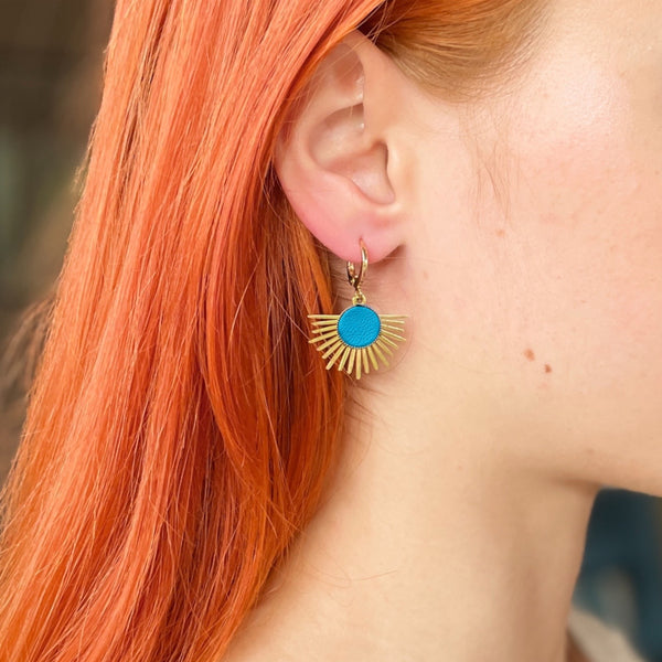 Petite boucle d'oreilles dorée Nune modèle Miria en acier inoxydable et laiton doré à l'or fin avec serti en cuir bleu turquoise satiné, portée à l'oreille par une femme aux cheveux roux