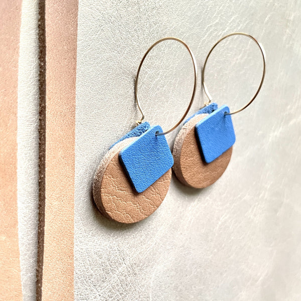boucles d'oreilles dorées Nune modèle Héra en cuirs beige amande et bleu denim mat sur fond gris doré, vues de côté