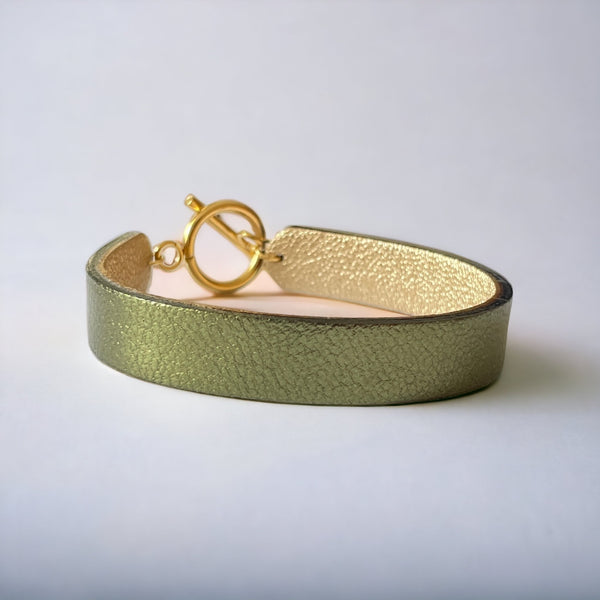 Bracelet en cuir double face bicolore avec cuir doré antique mat au verso et cuir kaki métallisé au recto avec fermoir boucle dorée en T, vu de face, sur fond gris