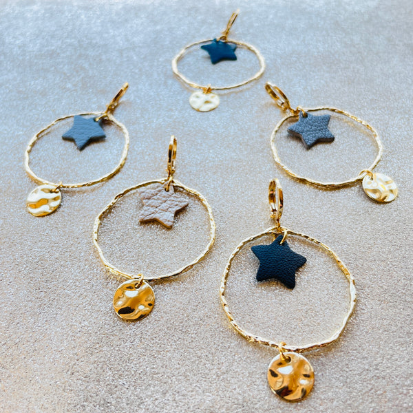 Boucles d'oreilles Nune modèle Naleli dorées à l'or fin de forme créole avec étoile de cuir coloré, vues de dessus, sur fond cuir beige pailleté