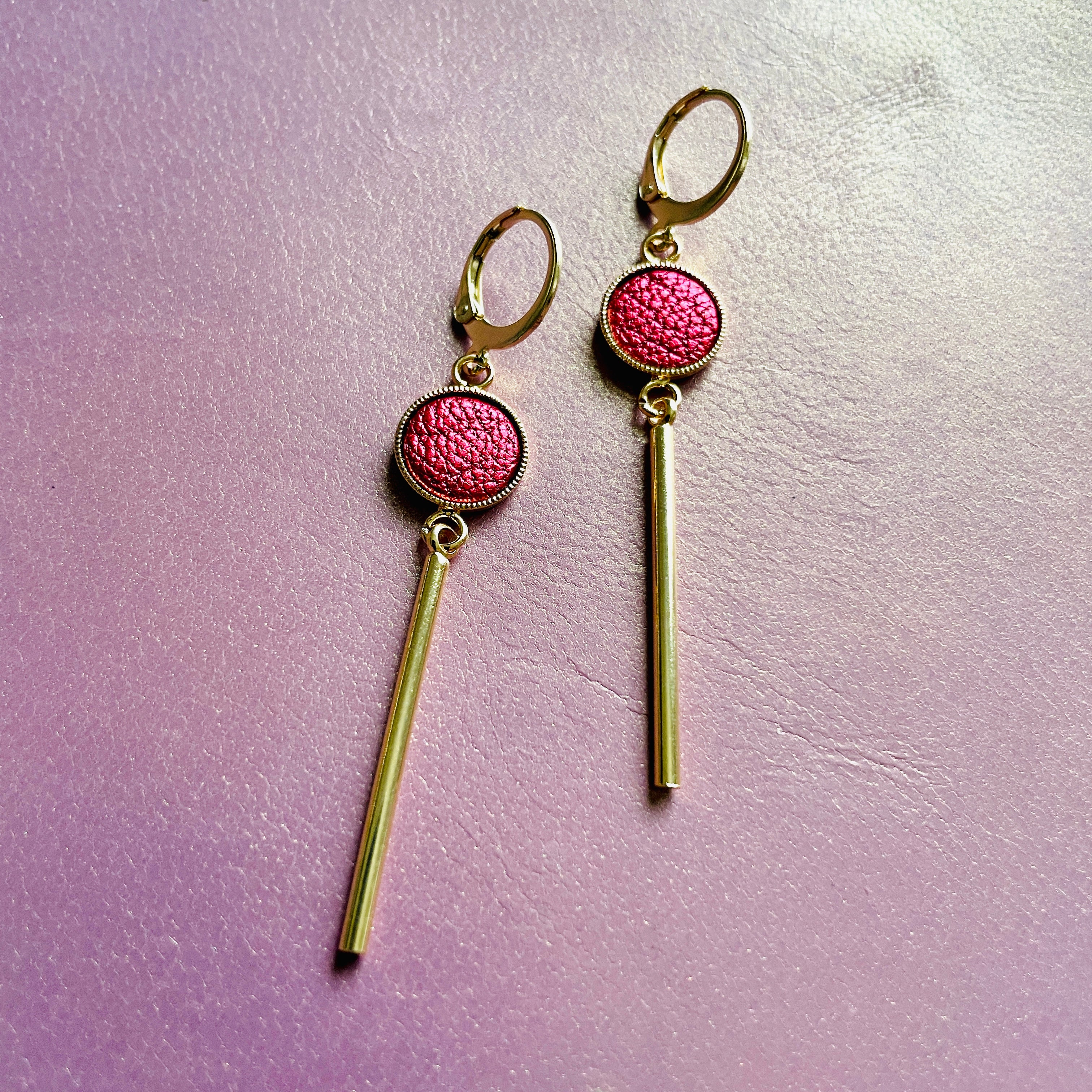 Nune longues et fines boucles d'oreilles dorées Nida avec serti en cuir rubis métallisé, sur fond cuir mauve irisé