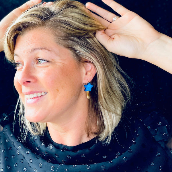 boucle d'oreille dorée Nune modèle Stella en forme d'étoile, en cuir bleu roi métallisé, portée à l'oreille