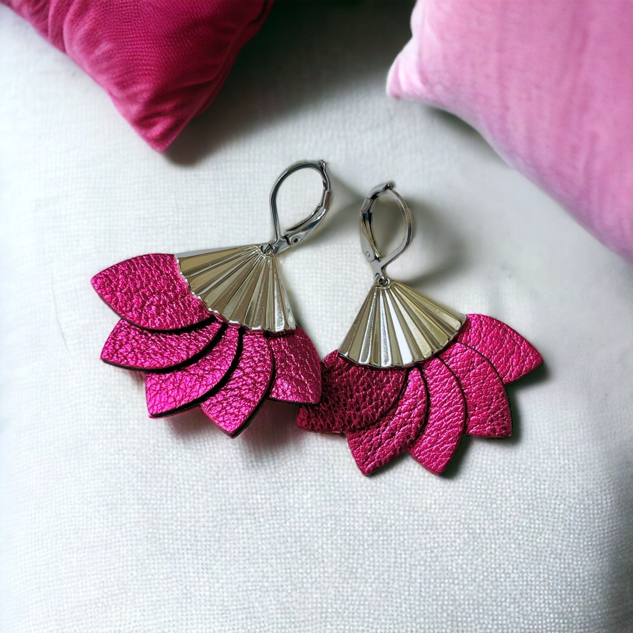Boucles d'oreilles argentées Nune modèle Sakura en pétales de cuir fushia métallisé, sur fond blanc avec coussins roses