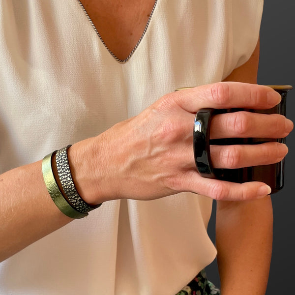 2 bracelets en cuir double face bicolores, avec fermoir boucle dorée en T, en cuirs noir grainé or pour le 1er, et kaki métallisé pour le second, portés au poignet