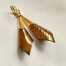 Charger l&#39;image dans la galerie, Boucles d&#39;oreilles dorées Nune modèle Alice en forme de cônes de cuir bronze brillant façon serpent, sur fond cuir blanc cassé nacré
