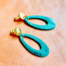 Charger l&#39;image dans la galerie, Puces d&#39;oreilles dorées Drys de la marque Nune, avec leurs anneaux ovales en cuir vert émeraude brillant, sur fond cuir corail nacré clair, vues de côté
