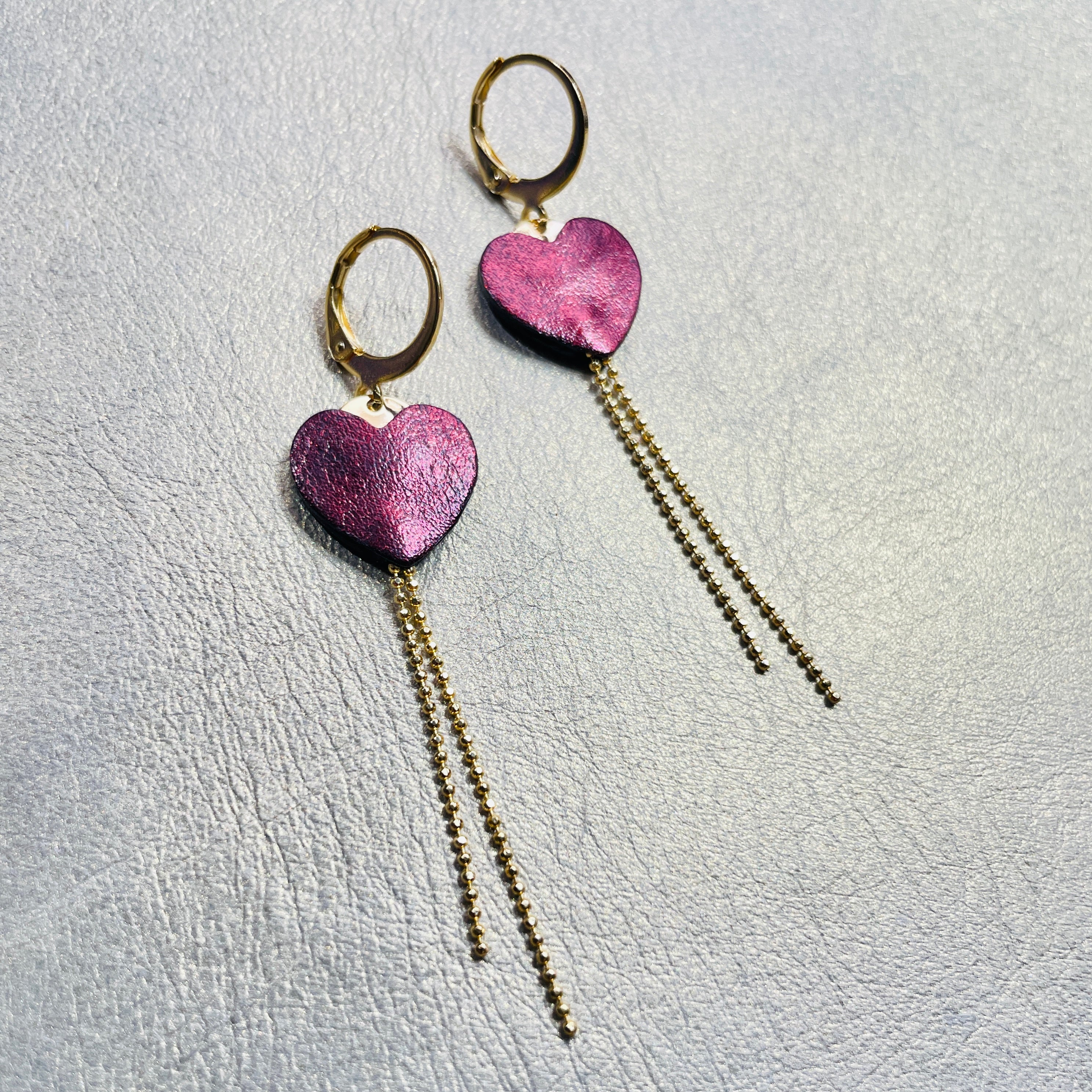NUNE fines boucles d'oreilles dorées, petits cœurs de cuir recyclé grenat métallisé et chaînettes, sur fond gris