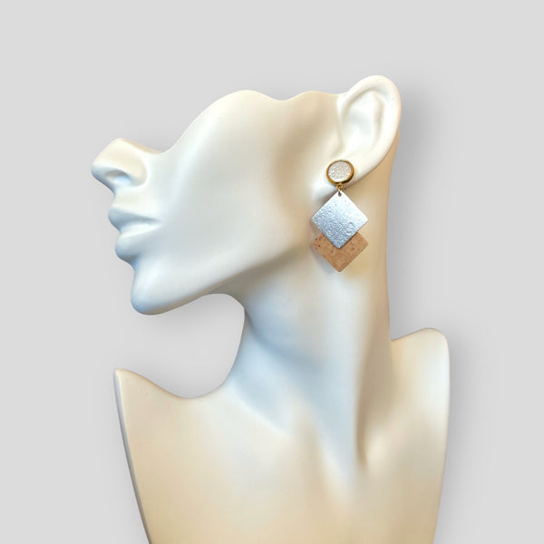 Boucle d'oreille dorée avec puce cabochon et duo de losanges en liège brut et argenté, portée à l'oreille
