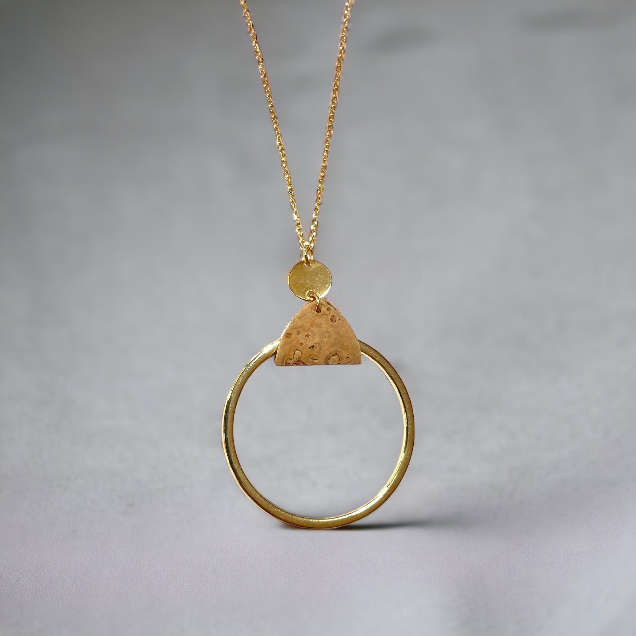 Collier fin dorée avec pendentif grand anneau créole attaché par une fine pièce de liège brut, sur fond gris